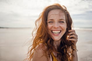 Minimalistisch reisen: Weniger Gepäck, mehr Erlebnis Portrait of a redheaded woman, laughing happily on the beach