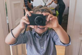 Lohnt es sich noch, für Kinder eine Fotokamera anzuschaffen? Young boy taking pictures digital snapshot camera indoor.