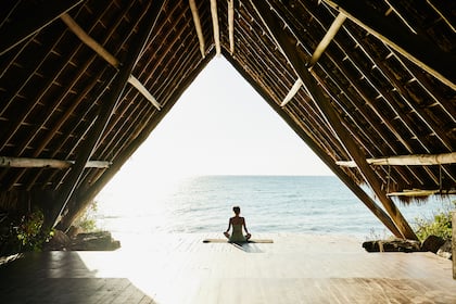 Destination Zen: Reisen für Körper und Geist Wide shot of woman relaxing after practicing yoga in ocean front pavilion at tropical resort