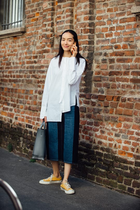 MILAN, ITALY - SEPTEMBER 21: Model Fei Fei Sun talks on the phone and wears an oversized white blouse, denim skirt, Acne Studios bag, and white Converse sneakers after the Salvatore Ferragamo show during Milan Fashion Week Spring/Summer 2020 on September 21, 2019 in Milan, Italy. (Photo by Melodie Jeng/Getty Images)