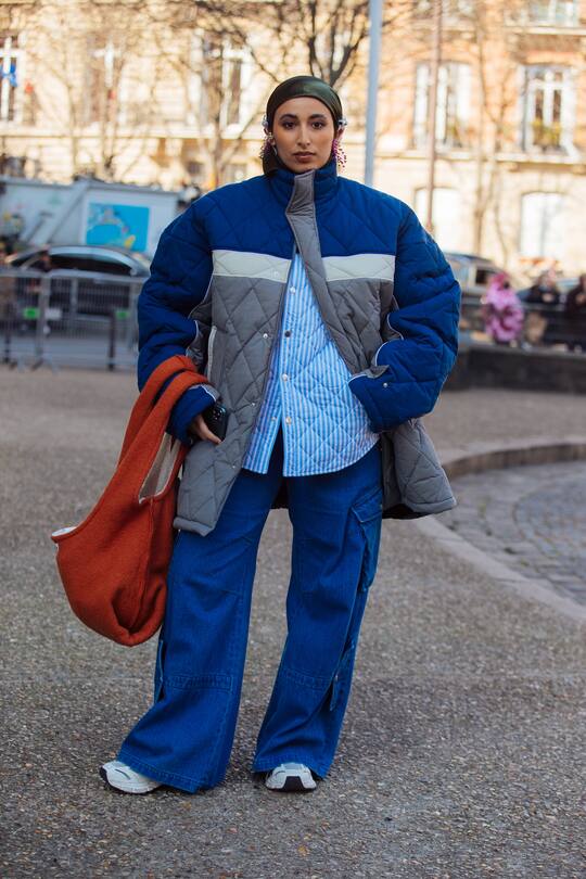 PARIS, FRANCE - MARCH 08: Taqwa Bintali wears a green head scarf, boxy blue and gray Egon Lab down jacket, blue and white striped top, boxy blue cargo pants, and oversized light brown purse, and white chunky sneakesr at the Miu Miu show at Palais d'Iéna during Paris Fashion Week Fall/Winter 2022 on March 08, 2022 in Paris, France. (Photo by Melodie Jeng/Getty Images)