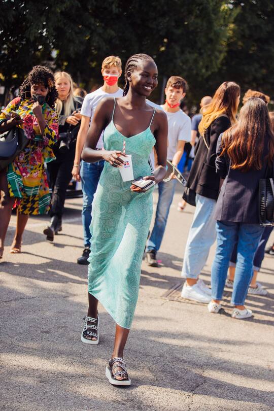 MILAN, ITALY - SEPTEMBER 23: Model Adut Akech wears a green Etro paisley slip dress and white Chanel studded sandals and holds a white Russell x Boss soda cup at the Boss x Russell Athletic show during the Milan Fashion Week - Spring / Summer 2022 on September 23, 2021 in Milan, Italy. (Photo by Melodie Jeng/Getty Images)
