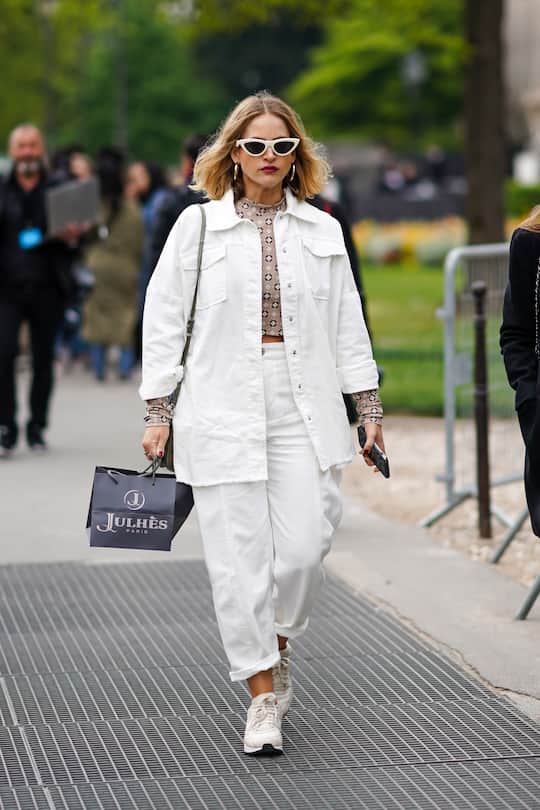 PARIS, FRANCE - MAY 03: A guest wears white sunglasses, a white jacket, earrings, white pants, sneakers, a brown cropped top with printed geometric patterns, outside the Chanel Cruise Collection 2020 At Grand Palais on May 03, 2019 in Paris, France. (Photo by Edward Berthelot/Getty Images )