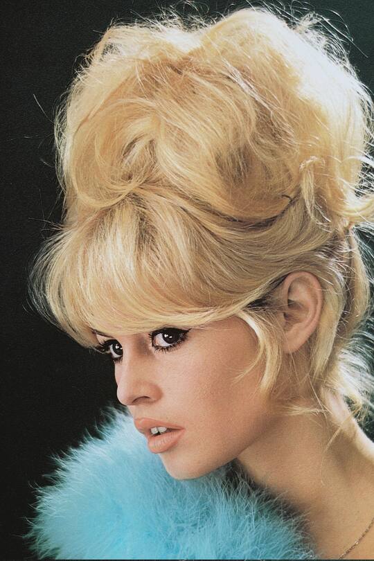 Headshot of Brigitte Bardot, French actress, model and singer, with a bouffant hairstyle and a blue boa in a studio portrait, against a black background, 1960. (Photo by Silver Screen Collection/Getty Images)