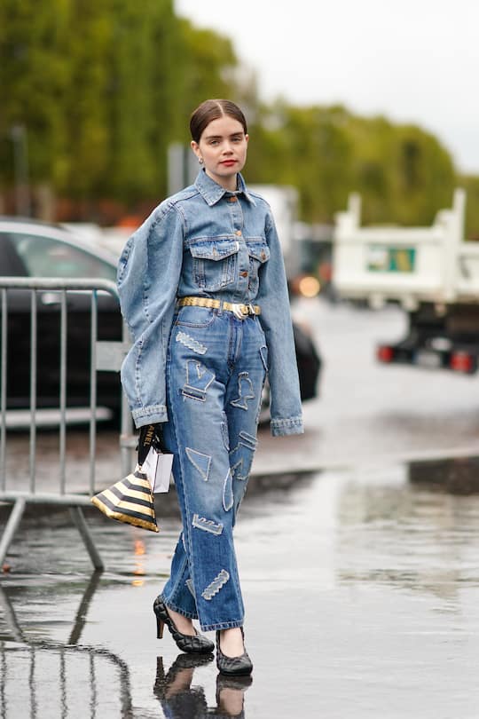 PARIS, FRANCE - OCTOBER 01: Reese Blutstein wears a blue denim oversized jacket with large pockets, a belt, blue denim jeans with patches, a golden and black striped pyramid bag, black quilted shoes, outside Chanel, during Paris Fashion Week - Womenswear Spring Summer 2020, on October 01, 2019 in Paris, France. (Photo by Edward Berthelot/Getty Images)