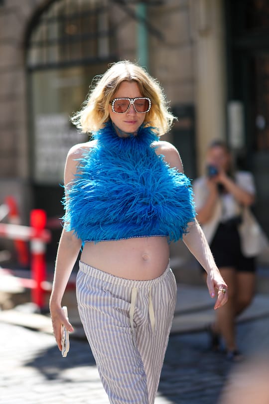 COPENHAGEN, DENMARK - AUGUST 11: A guest wears black and silver rhinestones large sunglasses, a blue feathers / halter neck cropped top, white striped print pattern large pants, outside Mark Kenly Domino Tan during Copenhagen Fashion Week Spring/Summer 2023, on August 11, 2022 in Copenhagen, Denmark. (Photo by Edward Berthelot/Getty Images)