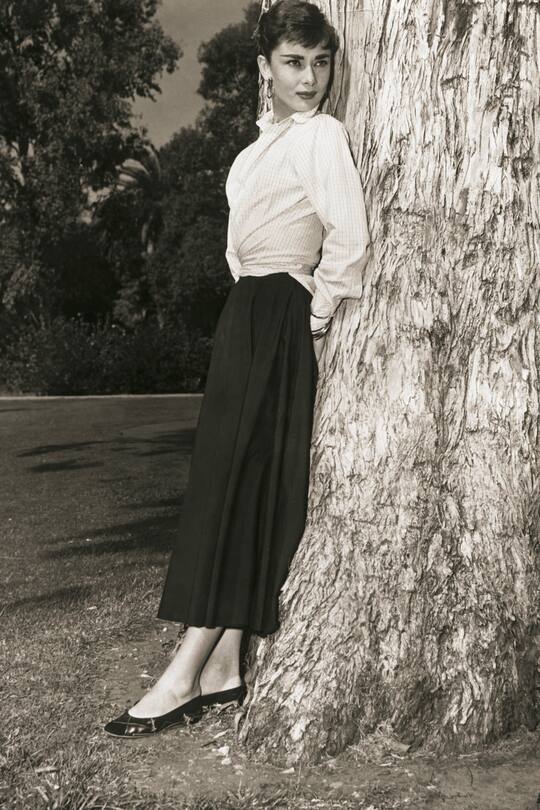 Belgian-born actress, Audrey Hepburn (1929-1993) standing against a tree in a publicity photograph circa 1950s.