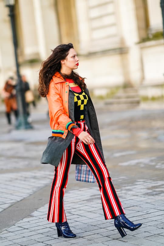 PARIS, FRANCE - OCTOBER 01: A guest wears an orange jacket with green buttons, black and red striped flare pants, leather shoes, a yellow and black top with printed checkered patterns, outside Louis Vuitton, during Paris Fashion Week - Womenswear Spring Summer 2020, on October 01, 2019 in Paris, France. (Photo by Edward Berthelot/Getty Images)