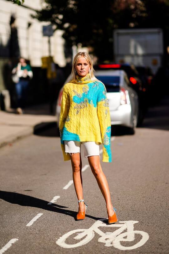A guest wears a blue and yellow wool pullover, white shorts, orange shoes, during London Fashion Week September 2018 on September 16, 2018 in London, England. (Photo by Edward Berthelot/Getty Images)