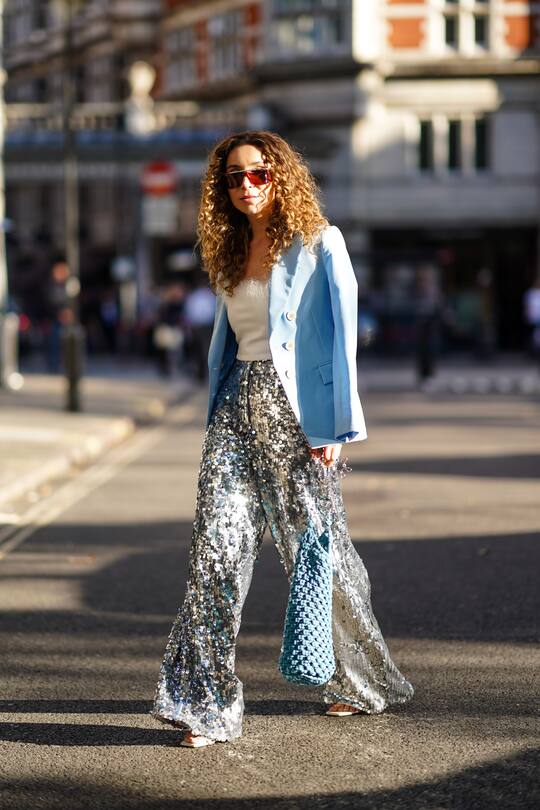 LONDON, ENGLAND - SEPTEMBER 13: Yasmine Daas wears a pale blue jacket, a white top, sunglasses, shiny sequined silver flare pants, a blue knitted bag, during London Fashion Week September 2019 on September 13, 2019 in London, England. (Photo by Edward Berthelot/Getty Images)