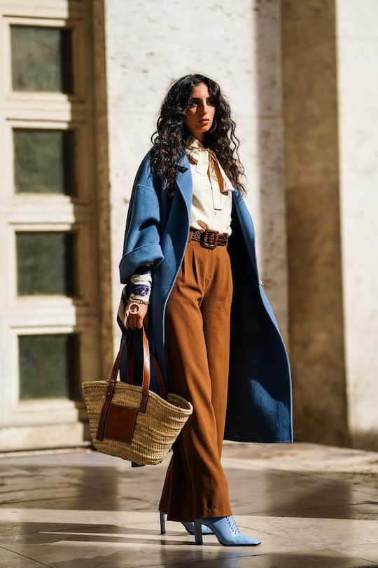 PARIS, FRANCE - SEPTEMBER 27: Gabriella Berdugo wears a blue coat, a shirt, a belt, brown flared pants, blue heeled shoes, a basket straw bag, outside Nina Ricci, during Paris Fashion Week - Womenswear Spring Summer 2020 on September 27, 2019 in Paris, France. (Photo by Edward Berthelot/Getty Images)