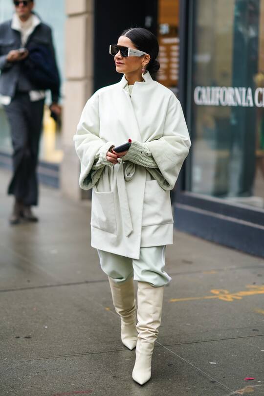 NEW YORK, NEW YORK - FEBRUARY 11: A guest wears sunglasses, a white oversized jacket, a wool pullover, leather pointy boots, earrings, during New York Fashion Week Fall Winter 2020, on February 11, 2020 in New York City. (Photo by Edward Berthelot/Getty Images)