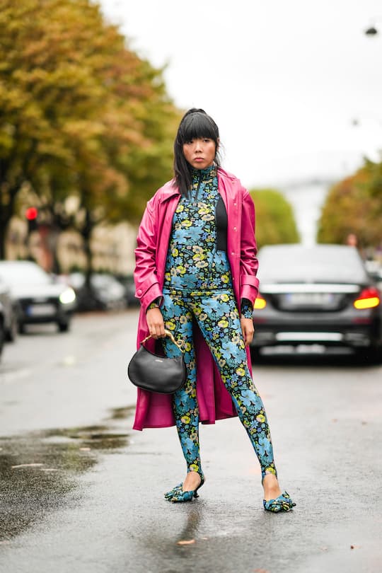 PARIS, FRANCE - OCTOBER 03: Susanna Lau wears a pink shiny vinyl long trench coat, a blue and yellow floral print jumpsuit with integrated stirrup leggings, a black Lanvin leather bag, pointed shoes with floral print, outside Lanvin , during Paris Fashion Week - Womenswear Spring Summer 2022, on October 03, 2021 in Paris, France. (Photo by Edward Berthelot/Getty Images)