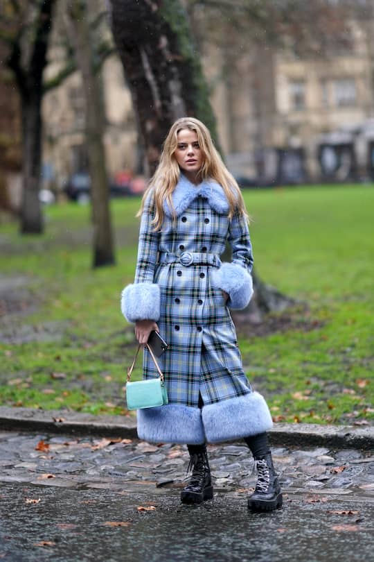 LONDON, ENGLAND - FEBRUARY 16: A guest wears a blue checked long coat with fluffy parts, a turquoise bag, a belt, black boots, leggings, during London Fashion Week Fall Winter 2020 on February 16, 2020 in London, England. (Photo by Edward Berthelot/Getty Images)
