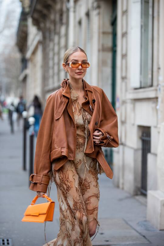PARIS, FRANCE - MARCH 02: Leonie Hanne seen wearing brown leather jacket, orange Acne bag, platform sandals, dress with print, sunglasses outside Acne during Paris Fashion Week - Womenswear F/W 2022-2023 on March 02, 2022 in Paris, France. (Photo by Christian Vierig/Getty Images)