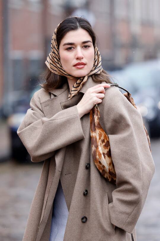 COPENHAGEN, DENMARK - FEBRUARY 01: Ilirida Krasniqi wearing a beige coat, a scarf and black boots, seen at the KERNE.MILK fashion show during Copenhagen Fashion Week Autumn/Winter 2022 on February 1, 2022 in Copenhagen, Denmark. (Photo by Streetstyleshooters/Getty Images)