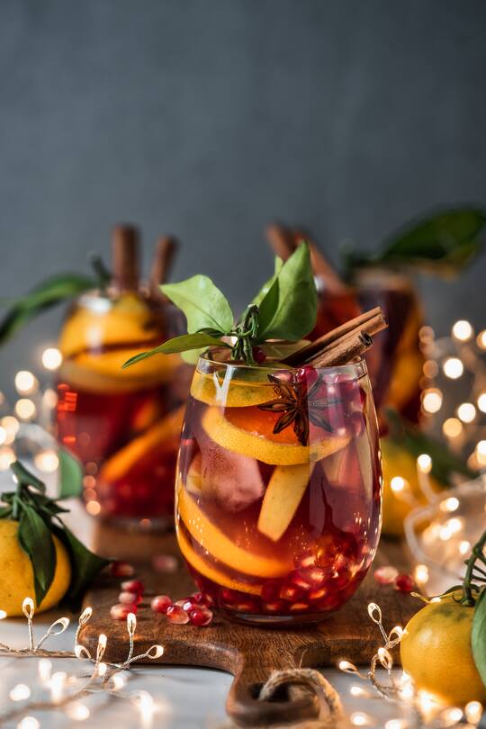 Winter sangria on dark christmas holiday background. Jugful of sangria and glasses with fruit slice, pomegranate and spices. Copy space for text or design. Vertical.