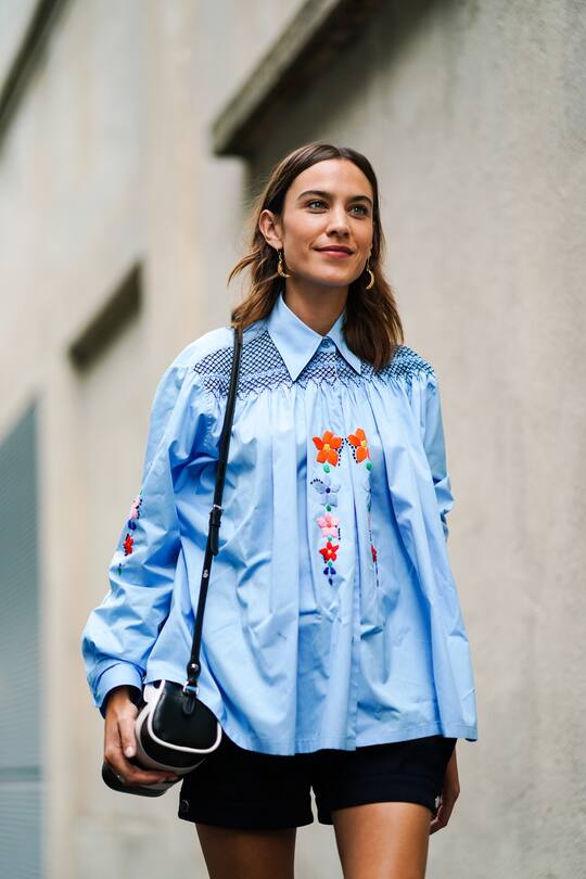 MILAN, ITALY - SEPTEMBER 18: Alexa Chung wears a blue pleated shirt with floral embroidery, earrings, outside the Prada show during Milan Fashion Week Spring/Summer 2020 on September 18, 2019 in Milan, Italy. (Photo by Edward Berthelot/Getty Images)