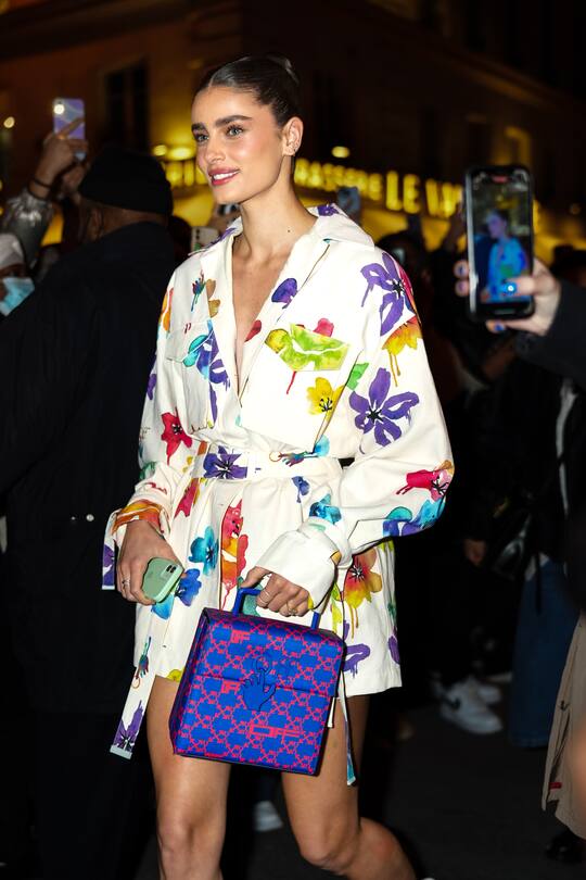 PARIS, FRANCE - FEBRUARY 28: Taylor Hill wears a white with multicolored large flower print pattern belted kimono jacket / dress, a blue with red monogram print pattern handbag from Off-White, silver rings, outside Off-White, during Paris Fashion Week - Womenswear F/W 2022-2023, on February 28, 2022 in Paris, France. (Photo by Edward Berthelot/Getty Images)