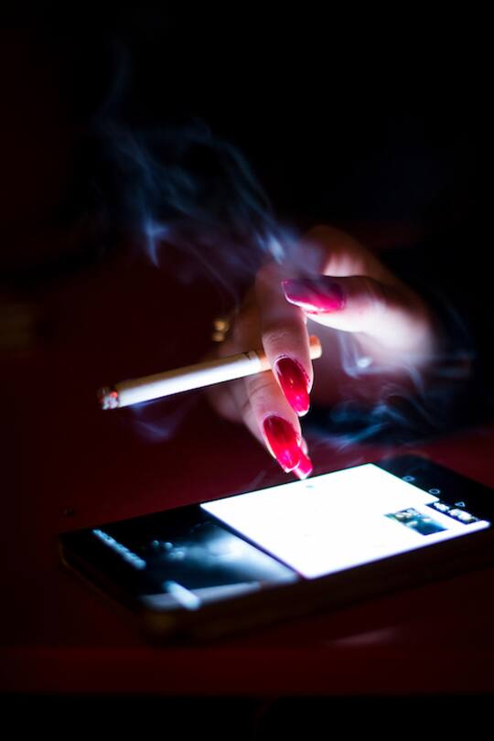hand with long red nails and cigarette on a mobile phone