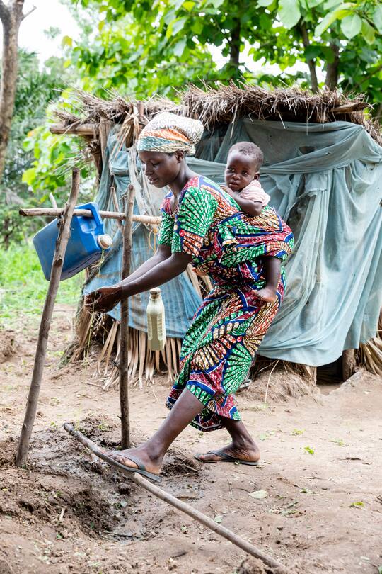 Yawa Mewezino, (27) und Tochter Clarissa (13 Monate), beim Händewaschen mit Asche und Wasser aus dem Tippy Tap. Im Dorf Aou Mono, Province Centrale, Togo, SRK, Schweizerisches Rotes Kreuz. Foto: Bernard van Dierendonck