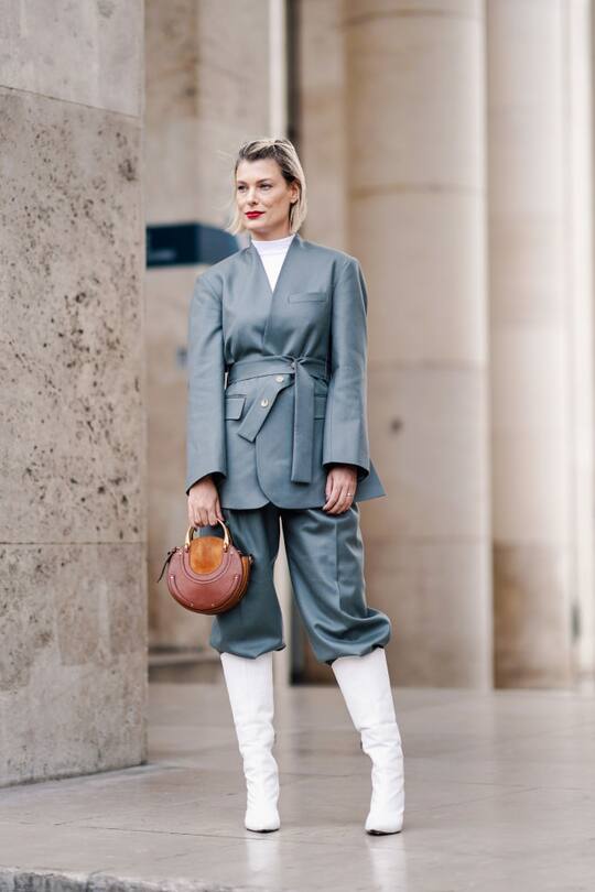 PARIS, FRANCE - FEBRUARY 28: A guest wears a blue wrap-over jacket, a white top, blue pants, black boots, a brown Chloé round bag, outside Atlein, during Paris Fashion Week Womenswear Fall/Winter 2019/2020, on February 28, 2019 in Paris, France. (Photo by Edward Berthelot/Getty Images)