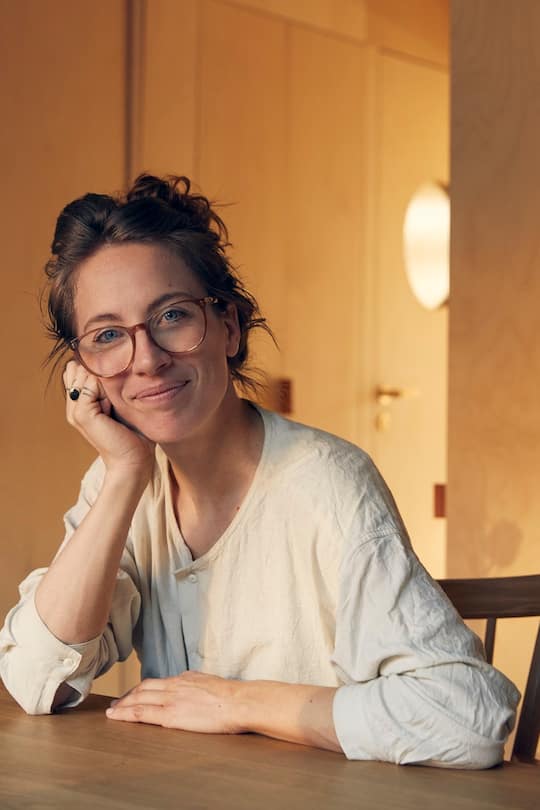 Woman with large glasses sitting on a table looking into camera