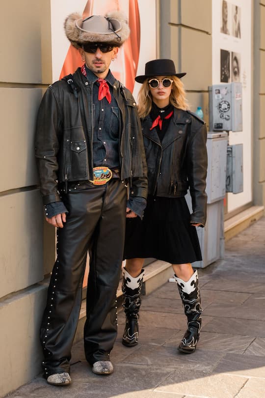 MILAN, ITALY - JANUARY 13: Guests wear blue denim shirt, black leather jacket and black leather pants, cowboy belt and taupe cowboy hat (L), and black leather jacket, black skirt, black and white cowboy boots and brown cowboy hat (R), outside MSGM, during the Milan Fashion Week - Menswear Fall/Winter 2024-2025 on January 13, 2024 in Milan, Italy. (Photo by Claudio Lavenia/Getty Images)