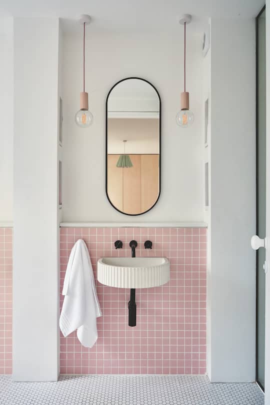 a bathroom interior held in white and rose with mirror and wash basin