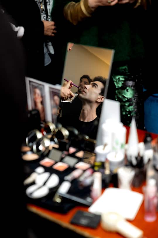a make up table backstage with a mirror, where a man is seen
