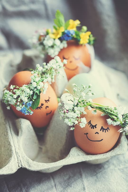 Natural easter eggs with funny painted face and sweet flower wreath