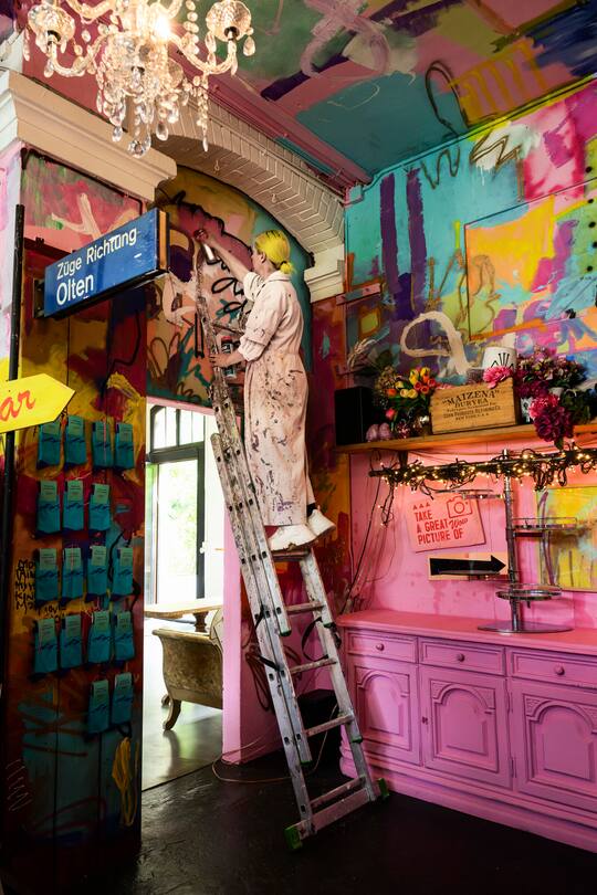 Barbara Kiener, Kuenstlerin, Performance Kuenstlerin, in ihrem Atelier, Kulturgarage, mit ihrer Schwester Simona Kiener, Mitarbeiterin Kulturgarage, Pink, Fahnenschwingen, Handoergeli spielen, Interlaken, 2023, Fotos: Geri Born