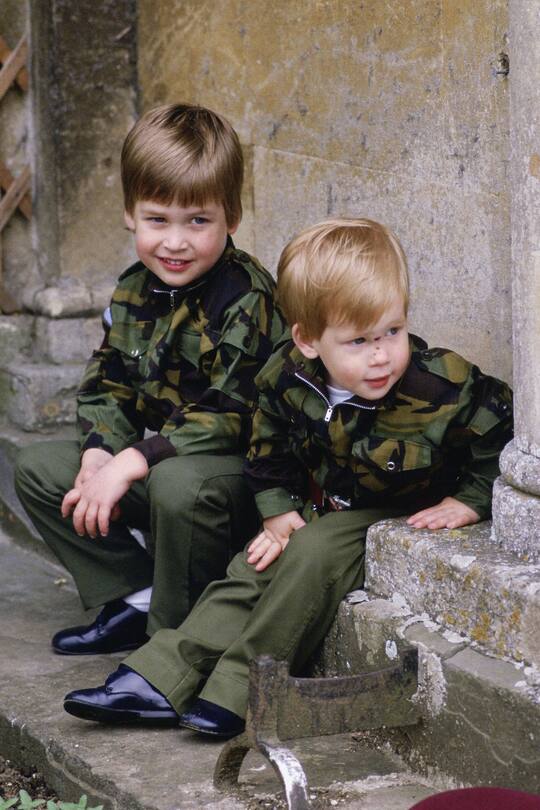 TETBURY, ENGLAND - JULY 18: Prince Harry and Prince William sit together on the steps of Highgrove House wearing army uniforms on July 18, 1986 in Tetbury, England. (Photo by Tim Graham Photo Library via Getty Images)