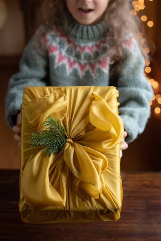 Little girl holding/giving a Christmas gift wrapped in silk.