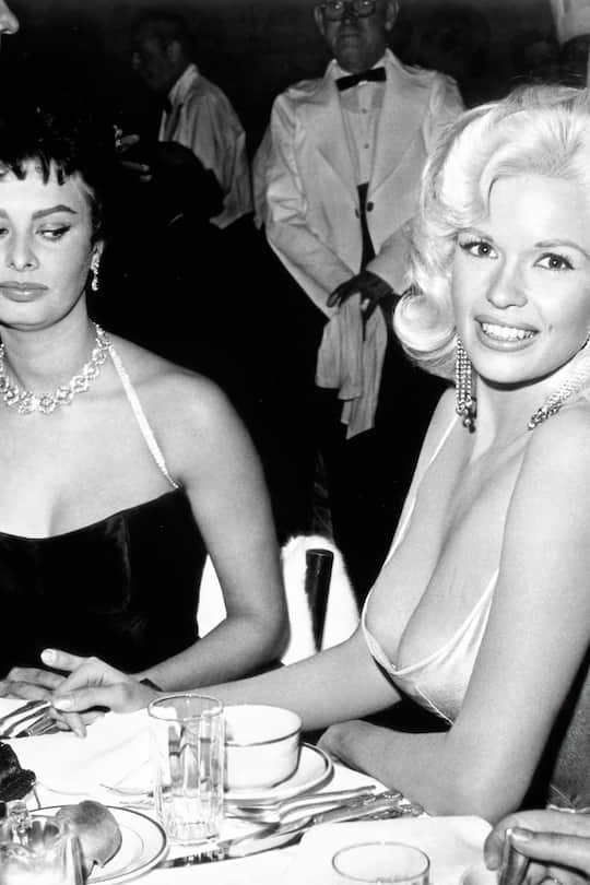 JAYNE MANSFIELD and SOPHIA LOREN. American actress and model Jayne Mansfield, known for her publicity stunts, attended a dinner at the exclusive Beverly Hills Romanoff's restaurant hosted by Paramount Pictures to officially welcome Italian actress Sophia Loren to Hollywood. A photograph of the two women, with Loren casting a sideways glance at Mansfield's cleavage, was distributed world-wide and became an international sensation.