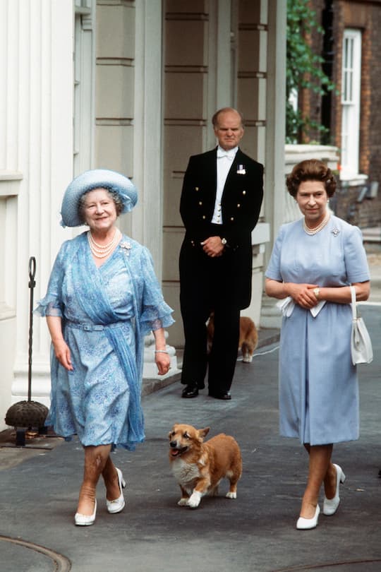 LONDON, UNITED KINGDOM - AUGUST 04: The Queen Mother, Smiling, With Her Daughter, Queen Elizabeth Ll, Outside Clarence House With Her Pet Corgi On Her 83rd Birthday. The Queen Mother Is Wearing A Blue Patterned Chiffon Dress And Blue Hat. (Photo by Tim Graham Photo Library via Getty Images)