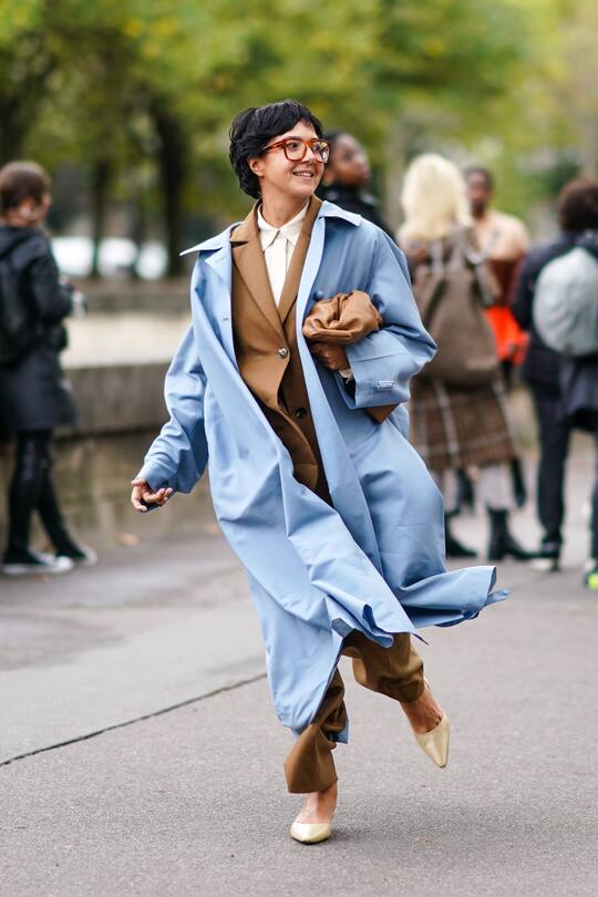 PARIS, FRANCE - SEPTEMBER 29: A guest wears a beige shirt, a camel jacket, camel pants, a camel puff clutch, a light blue oversized trench coat, lustrous beige shoes, outside Valentino, during Paris Fashion Week - Womenswear Spring Summer 2020, on September 29, 2019 in Paris, France. (Photo by Edward Berthelot/Getty Images)