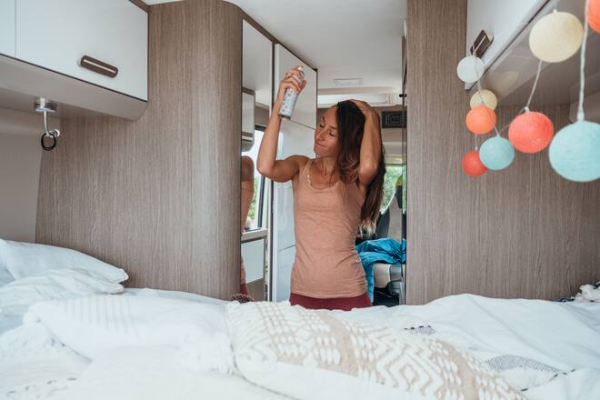 Road trip concept, woman living the van life experience. She sprays her hair at the back of her camper