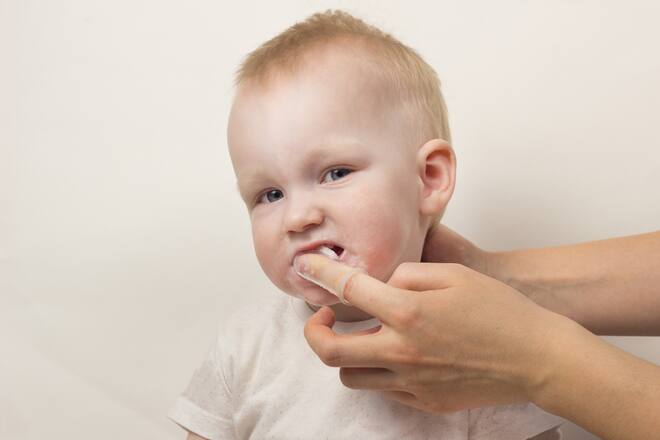 Mother cleans the teeth of a little girl, close-up