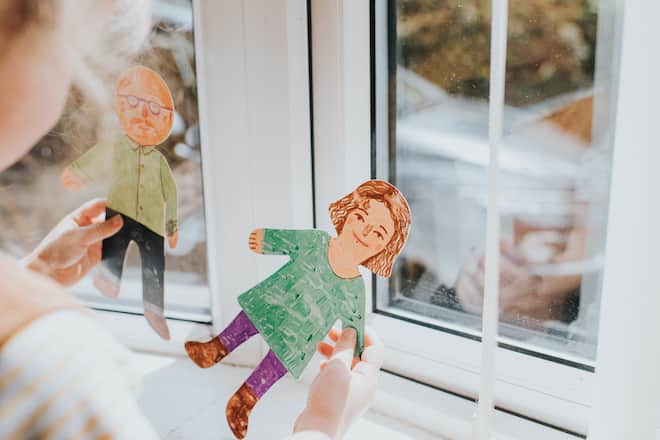 Little girl in a sunny room holding two paper people, one female, one male. Conceptual with space for copy.