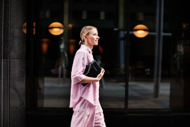 Stylish fashion woman in a pink suit, shirt and shorts walking confidently against a city backdrop. Urban street style allure.