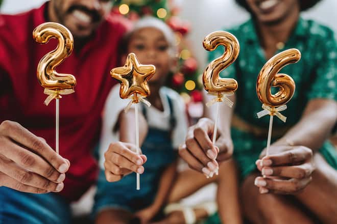 Festive family celebrating the new year at home, holding golden balloons with the numbers 2026. Christmas tree and holiday decorations in the background, joyful and warm atmosphere. Concept of family togetherness, holidays, festive season, new beginnings, 2026 celebration