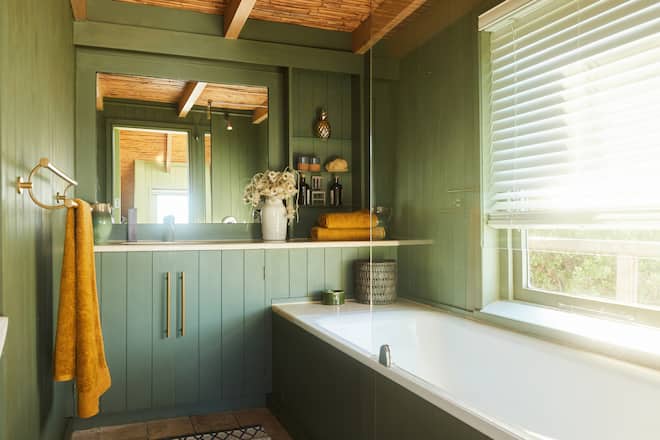 Bathtub and counter in a bathroom with green wood-paneled walls in a holiday home