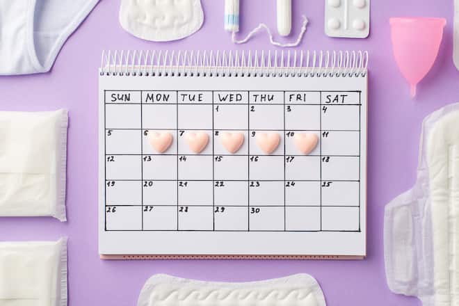 Top view photo of small pink hearts marks on the calendar panties pink menstrual cup painkiller pills hygienic pads and tampons on isolated pastel violet background