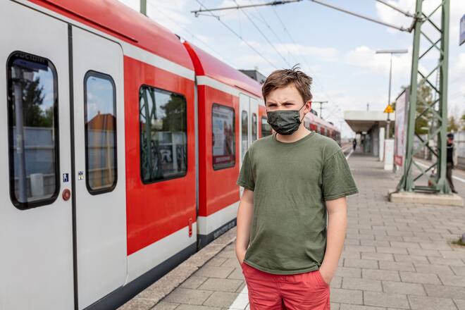 Teenager mit Corona-Maske neben Zug