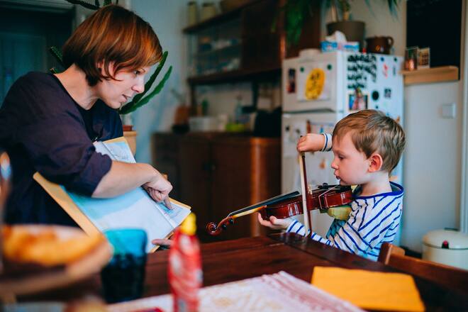 Young boy using violin while his mother showing him notes.
