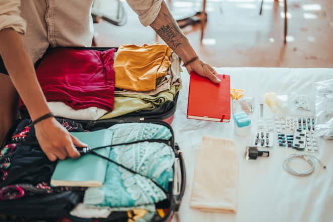 An unrecognizable man packs clothes and all the necessities for traveling in a suitcase.