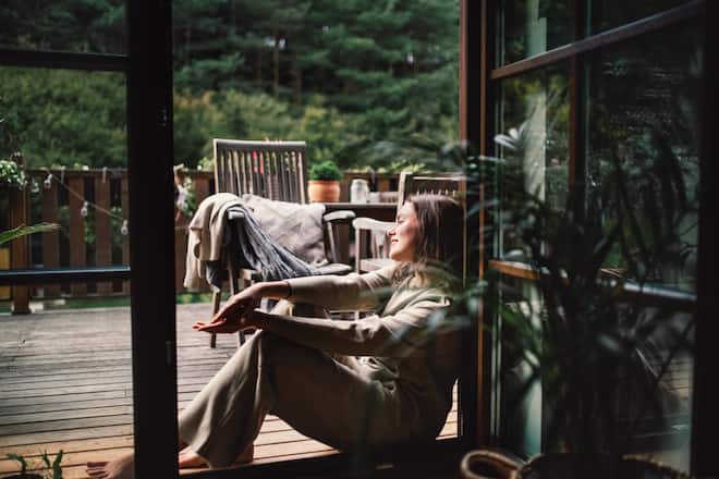 Woman resting in doorway of balcony doors, resting. Single woman enjoying free weekend. Concept of selfcare.