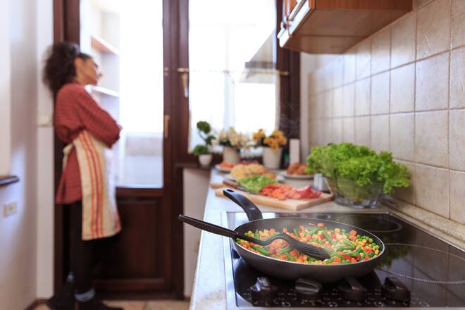 Pensive woman standing arms crossed in kitchen and looking through window.