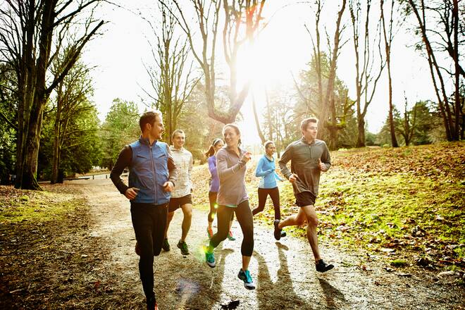 Smiling group of male and female runners trail running together in park